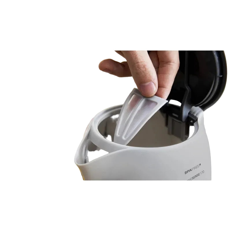 Hand using a spatula to remove a lid from a white appliance with a blurred background of a glass of orange juice and a colorful plate.
