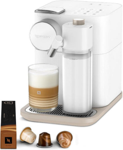 White Nespresso coffee machine with a glass of layered coffee and capsules on a white background