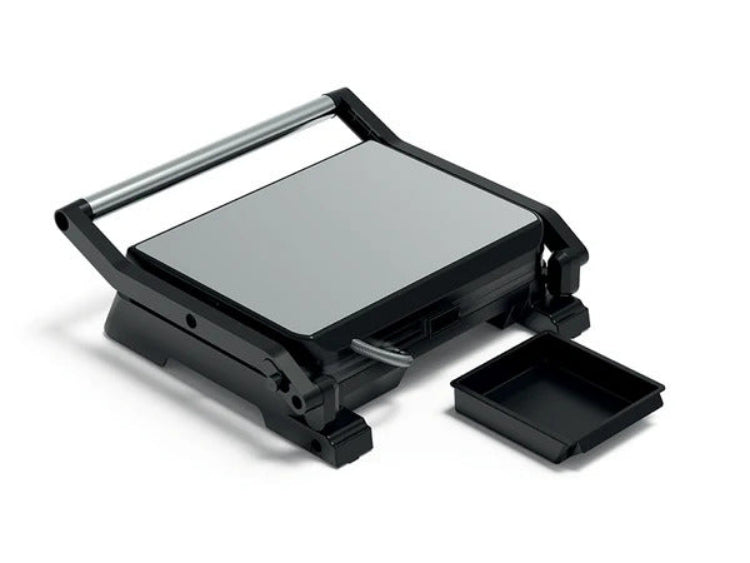 A black electric grill press with a silver heating plate, shown open with its handle raised and a small black tray beside it on a white background.