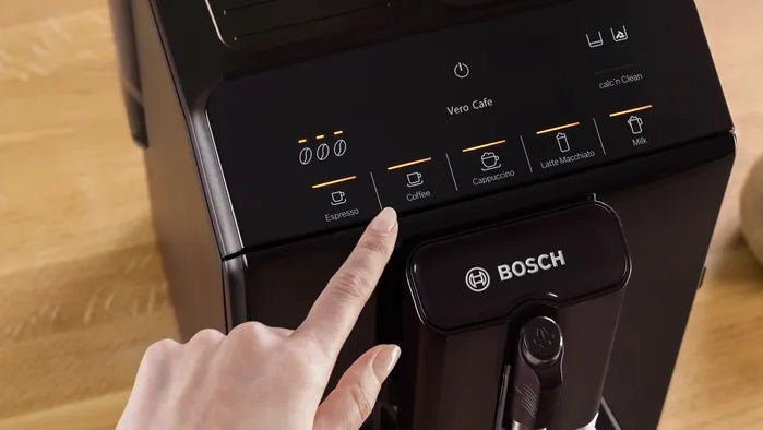 Bosch coffee machine with a hand pressing a button on a wooden surface