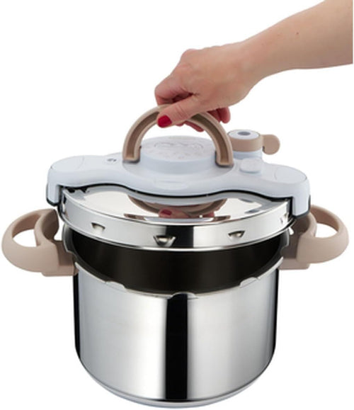 Stainless steel pressure cooker with beige handles held by a hand on a white background