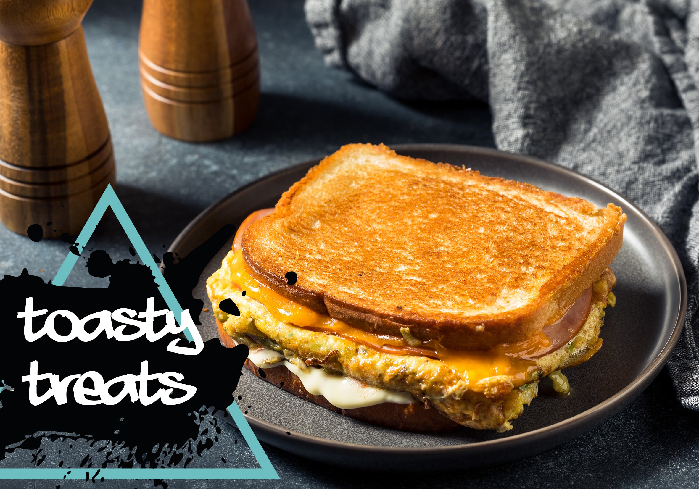 Grilled cheese sandwich on a black plate with 'toasty treats' text and pepper grinder in the background.